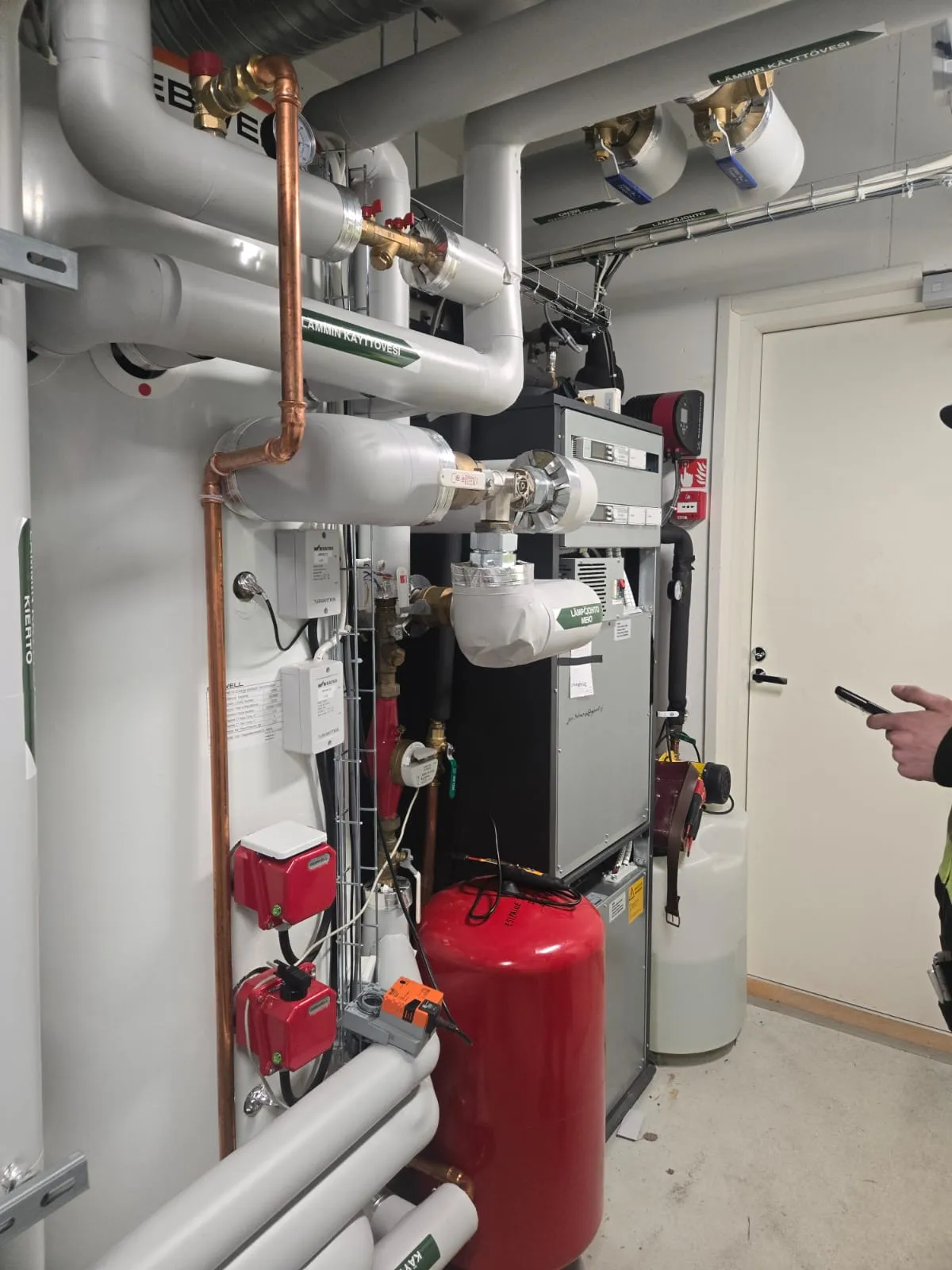 Laitetila, jossa on putkia, venttiileitä, pumppuja ja säiliöitä, valaistus on kirkas ja värit ovat pääosin harmaata, valkoista ja punaista.